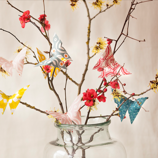 Decorative birds on branches with flowers in a glass vase against a neutral background