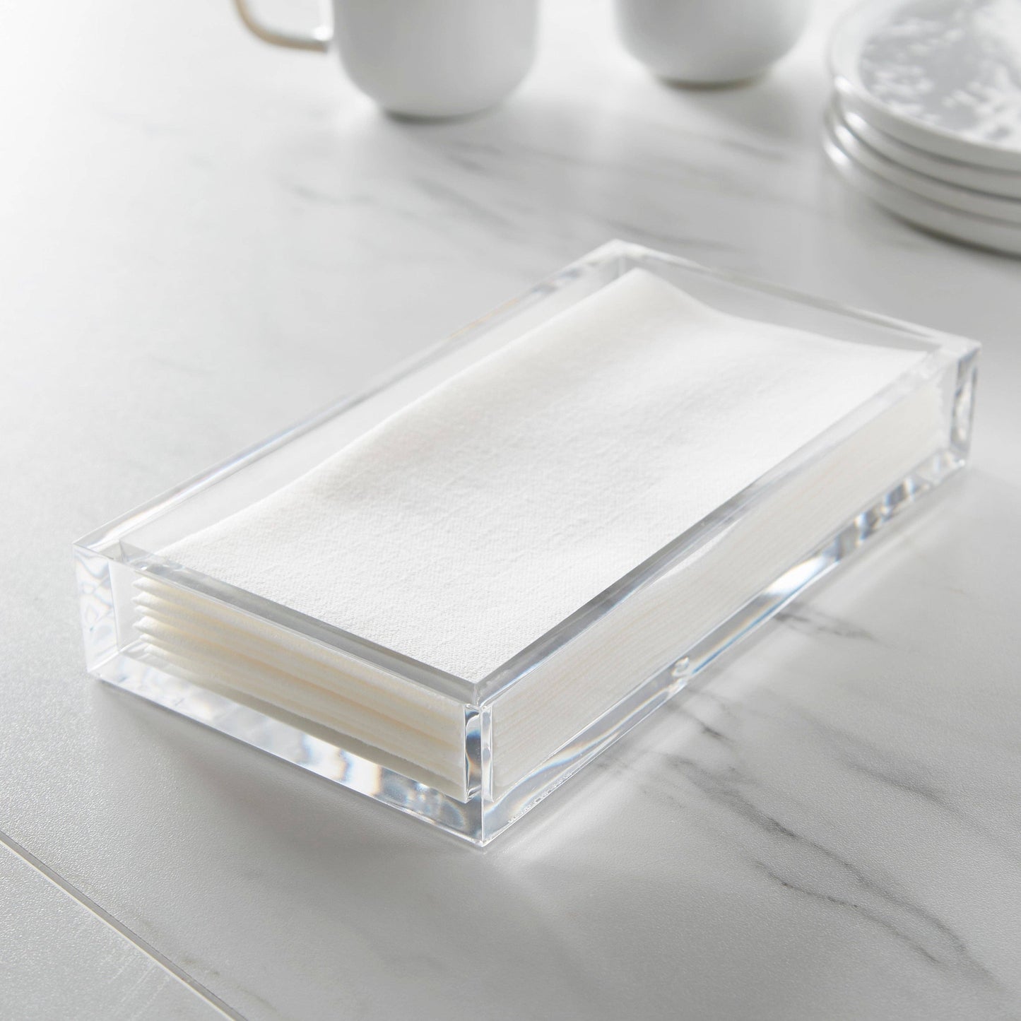 Clear acrylic napkin holder with white napkins on a marble surface