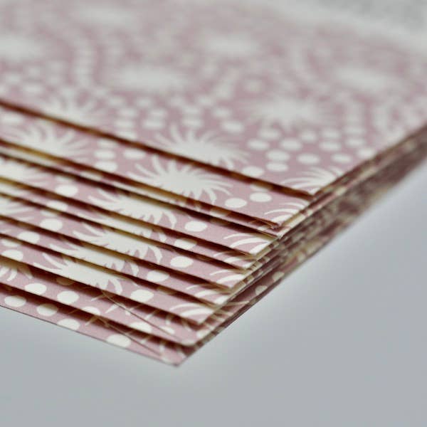 Stack of pink paper with white floral pattern on a light gray background