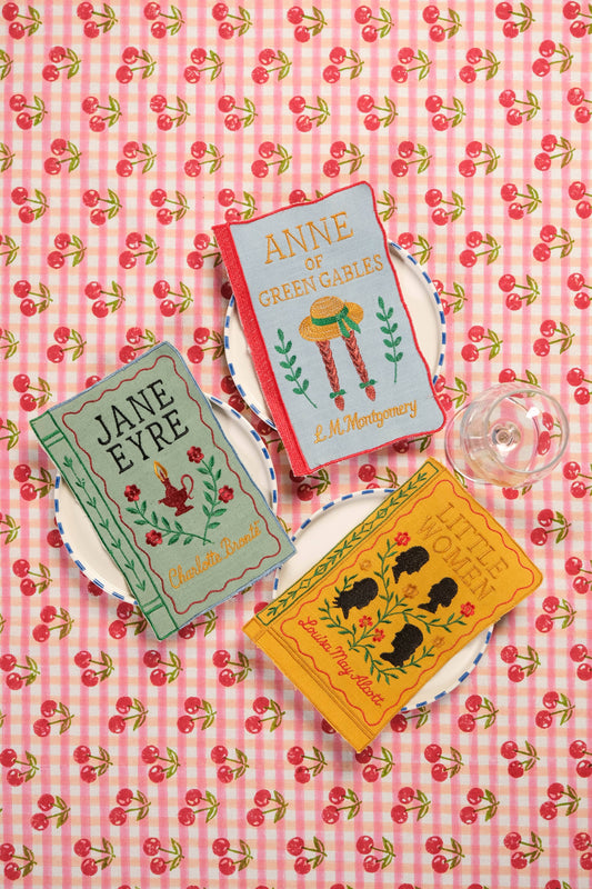 Three books on a pink checkered tablecloth with cherry pattern