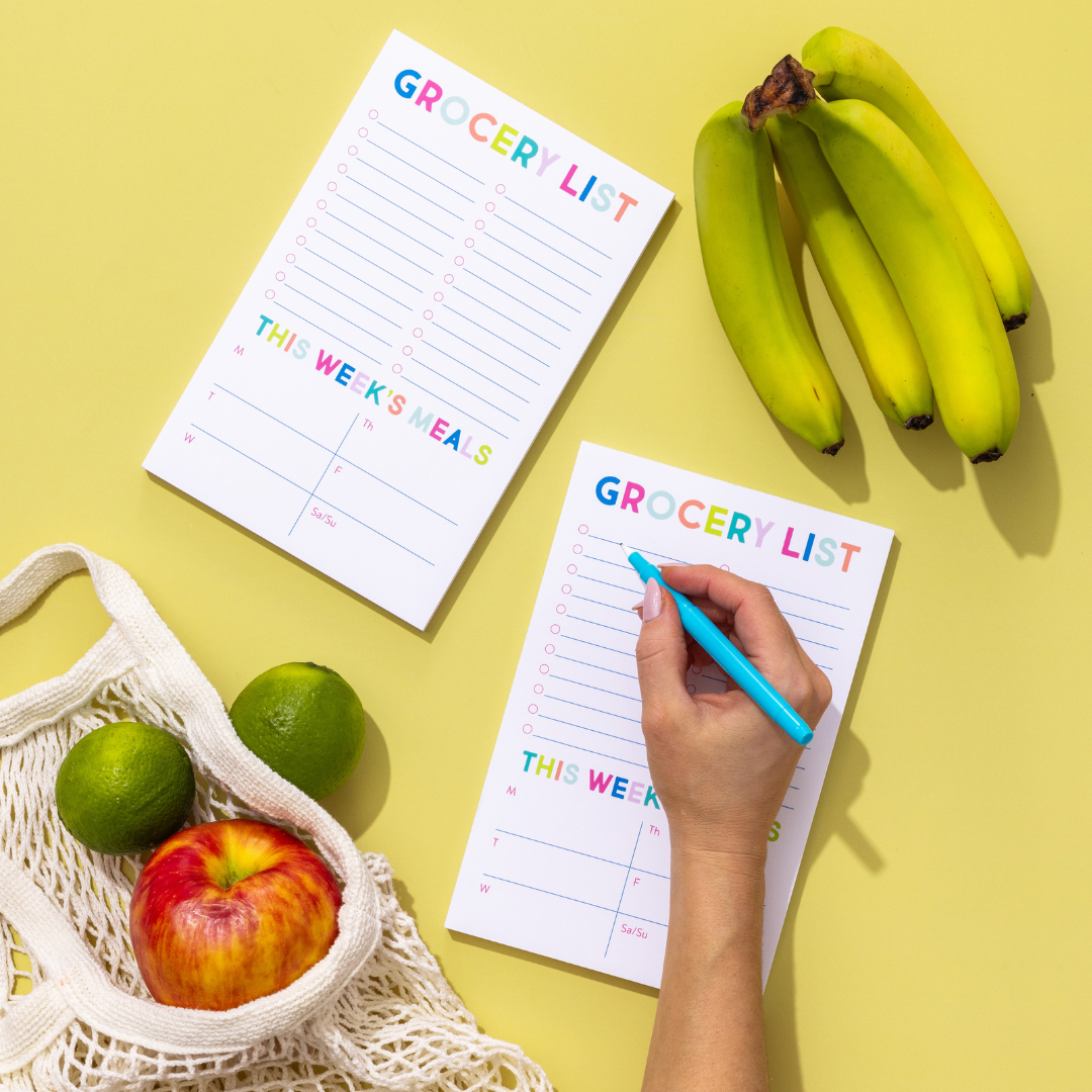 Person writing on a grocery list with fruits and a basket on a yellow background