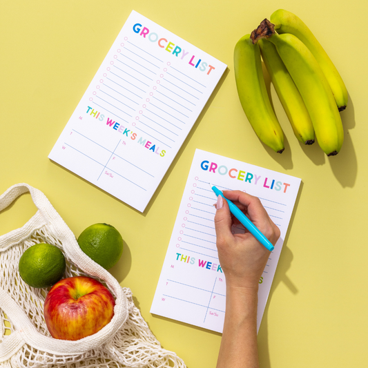 Person writing on a grocery list with fruits and a basket on a yellow background