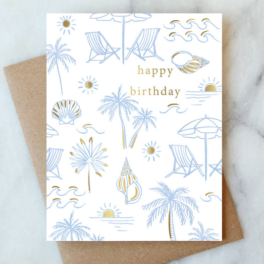 Birthday card with beach-themed illustrations and 'happy birthday' text, placed on a marble surface.