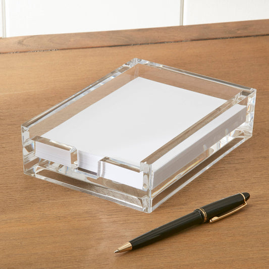 Clear acrylic notepad holder with white paper on a wooden surface, accompanied by a black pen with gold accents.