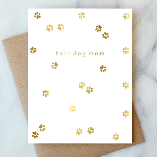 Greeting card with 'best dog mom' text and gold paw prints on a white background, placed on a marble surface.