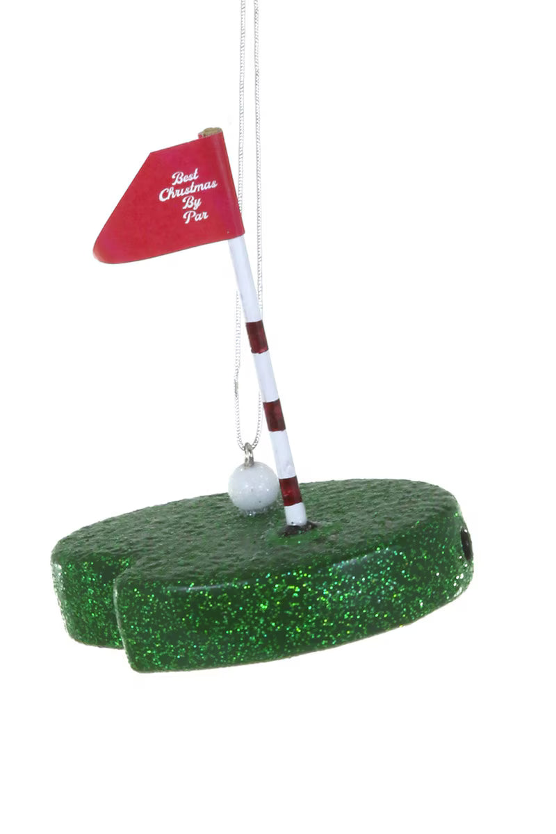 Golf ornament with red flag and white ball on a green base against a white background