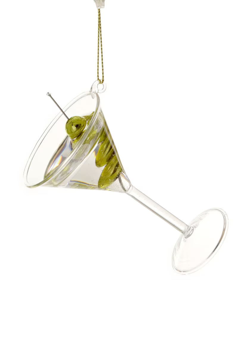A clear glass martini-style hanging ornament shaped like a tilted cocktail glass with green olives on a skewer, shown against a plain white background.