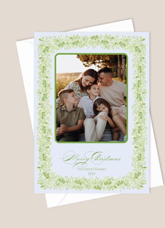 Christmas card with a family photo and green border with greenery and blue background