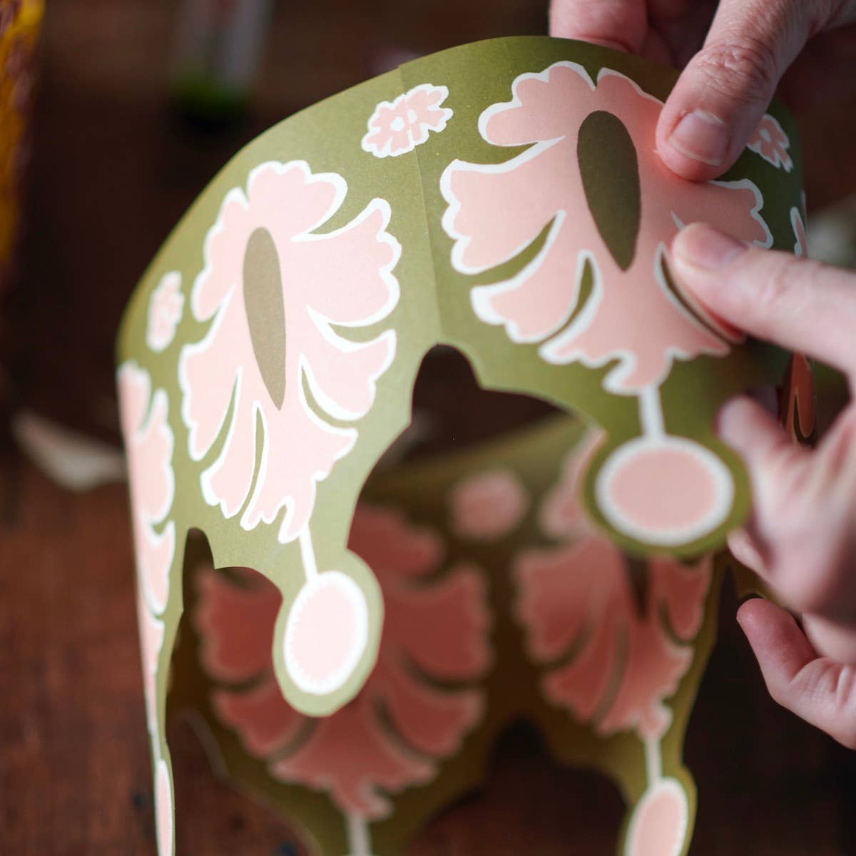 Hand holding a decorative paper cutout of a fish with floral patterns.