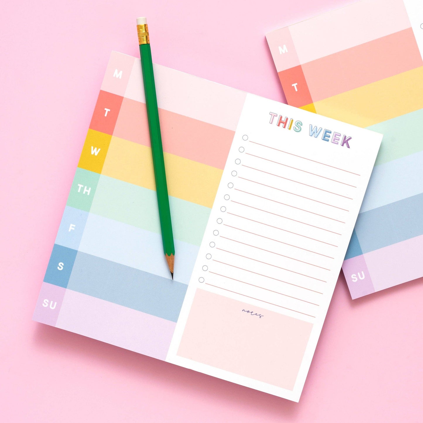 Colorful weekly planner notepad with a green pencil on a pink background