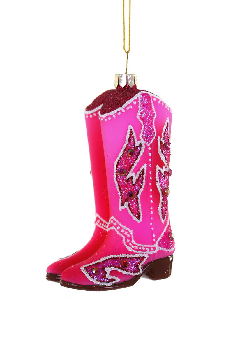 A pink cowboy boot Christmas ornament with sequined western-style designs, hanging by a gold string against a white background.