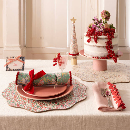 Decorative table setting with a cake, crackers, and place settings on a floral tablecloth.