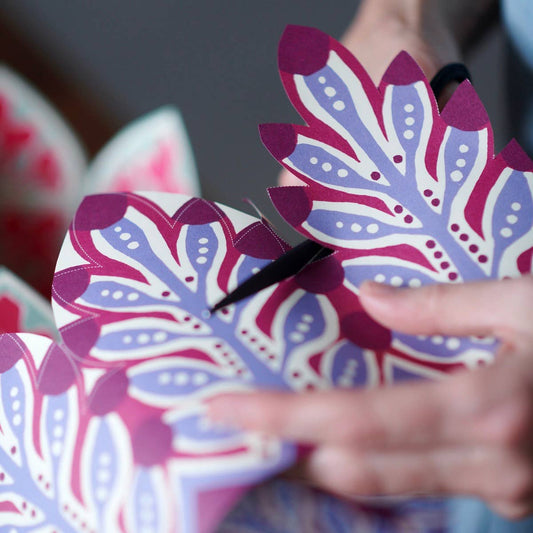 Person cutting out a purple and pink floral paper cutout with scissors.