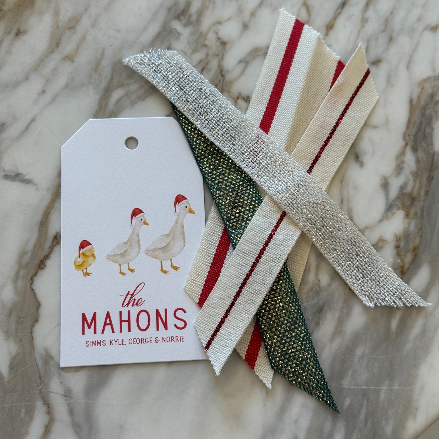 white paper tag printed with 'the MAHONS' and duck illustrations, displayed on a light gray marble surface.