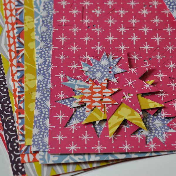 Colorful paper with geometric cut-out shapes on a pink patterned background
