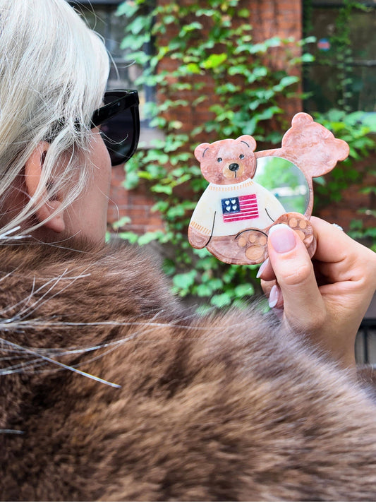 Person holding a decorative bear ornament with an American flag design outdoors.