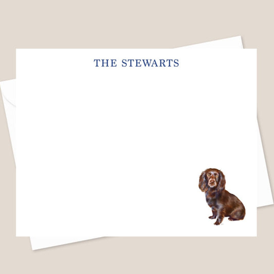 A personalized stationery set with a flat note card and an envelope, featuring an illustration of a dog on the front of the card, and the name 'THE STEWARTS' printed at the top. The envelope has a plain design.